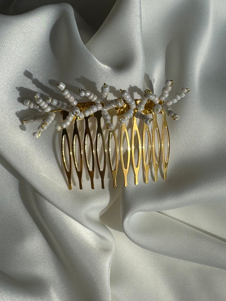 A gold hair comb with pearl floral accents, displayed on draped white satin fabric.
