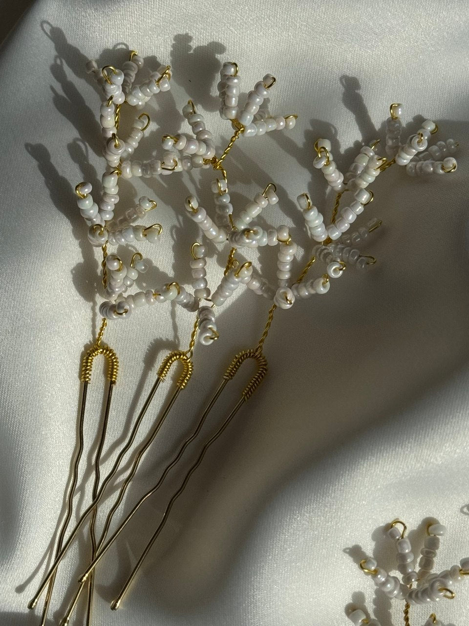 White beaded hair sticks with gold wire handles and pins, arranged on a white fabric background.