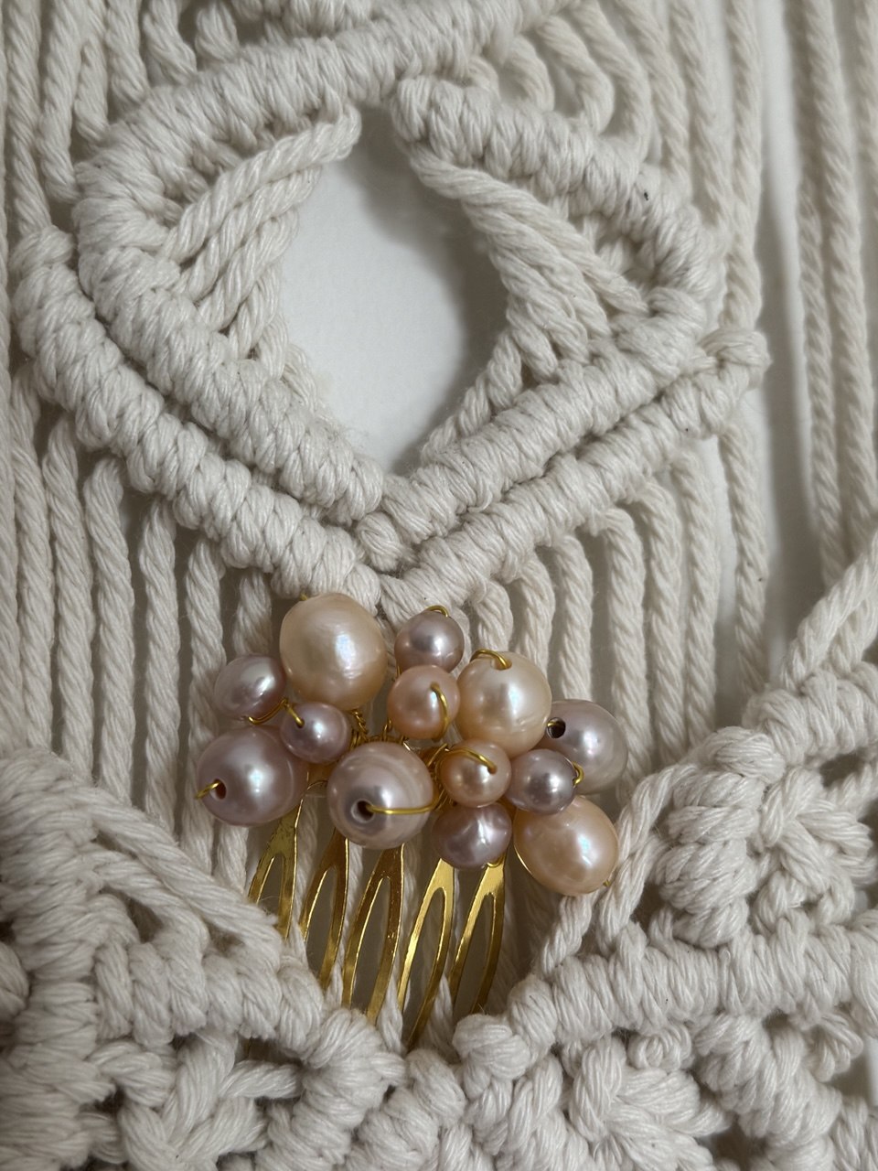 A close-up of a gold hair comb embellished with clustered  pearls in soft pink, beige, and cream tones 